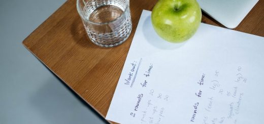 A green apple, glass of water, and workout plan on a wooden desk symbolize healthy living.